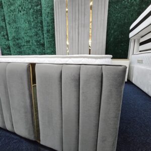 Headboard close-up of grey velvet bed with gold trim and panel stitching